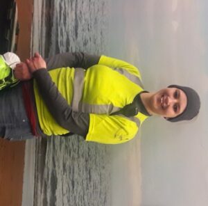 Woman with reflective vest standing next to ocean.