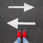 Red sneakers on the asphalt road with drawn arrows pointing to two directions - use a staffing agency vs. apply directly to an employer