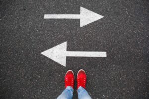 Red sneakers on the asphalt road with drawn arrows pointing to two directions - use a staffing agency vs. apply directly to an employer