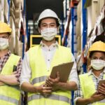 Three warehouse workers wearing masks with clipboards