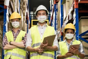 Three warehouse workers wearing masks with clipboards