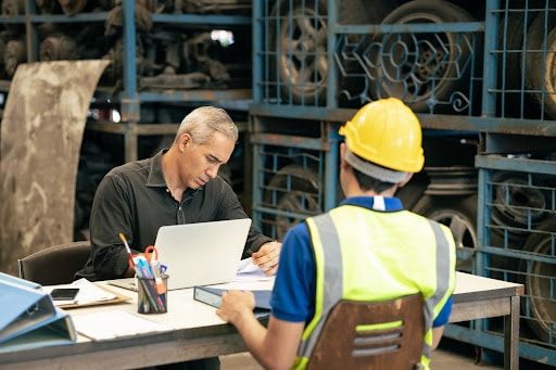 Man in a hard hat sitting at a desk with his manager